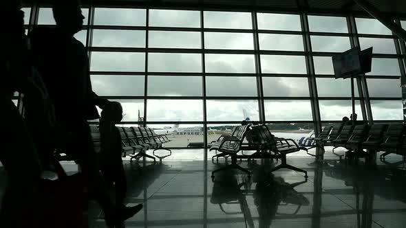 Travelers Walking Along Window in Airport Terminal, People Silhouettes Walking.