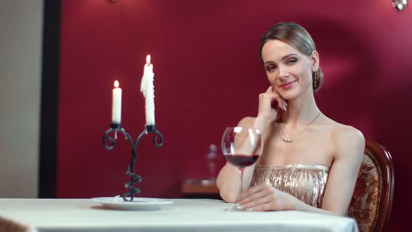 Elegant Smiling Woman in Luxury Clothing Sitting on Table with Candles