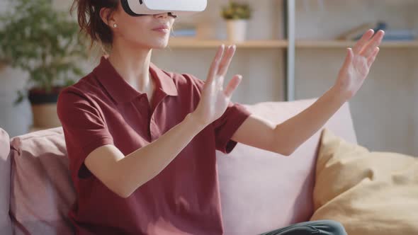 Young Woman in VR Headset Sitting on Sofa and Touching Air