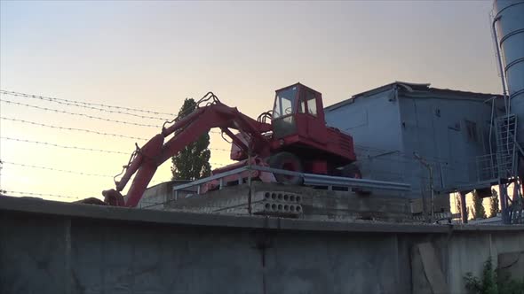 A Red Excavator Stands on a Platform Near the Plant. Storage Earthmoving Machine Behind Barbed Wire