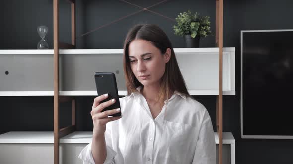 Young Businesswoman in a White Shirt Holding a Smartphone Smiling Straightening Her Hair Making a