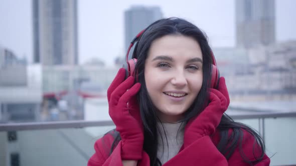 Close-up Face of Smiling Young Caucasian Girl with Black Hair and Green Eyes Putting on Earphones