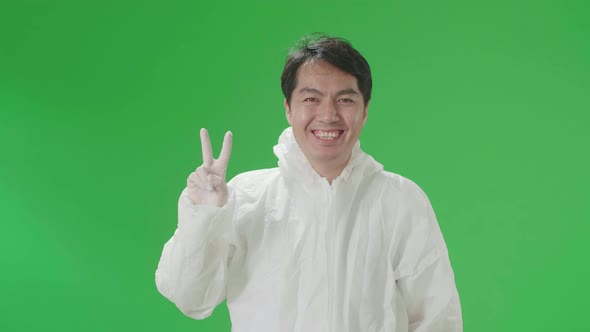 Male Wear Protective Uniform PPE Take Off Mask And Smiling With Victory Hand Sign In Green Screen