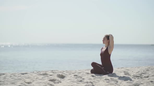 Young Beautiful Woman Practicing Yoga on the Beach at Sunny Day