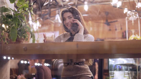 Young Brunette Woman in Harness Viewed Through Window of Cafe Dials a Number and Starts Talking on