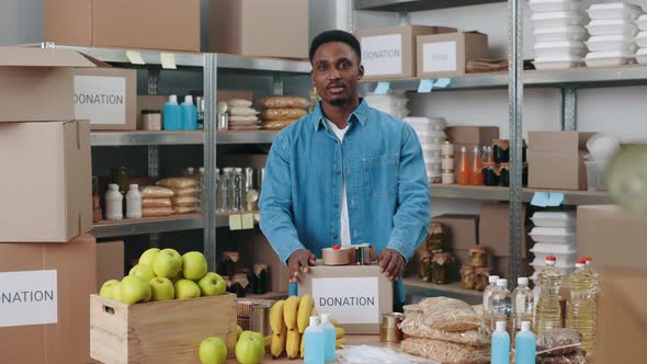 African Guy Standing at Warehouse with Food for Donation