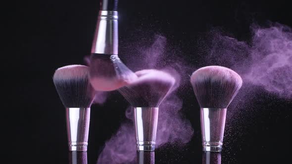 Beauty Concept. Cosmetic Brushes with Pink Cosmetic Powder Spreading on Black Background in Slow