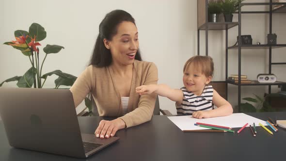 Mother and Her Little Daughter Looking at Laptop Together in Home Office
