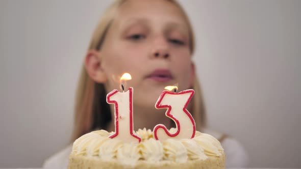 Cute Girl Blows Out the Candles Number Thirteen on a Birthday Cake
