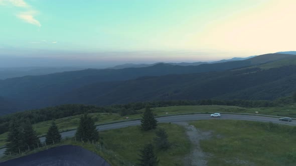 Two Cars Taking a Big Turn on Mountain Passage Road Against Forested Hills Deep Valley and Beautiful