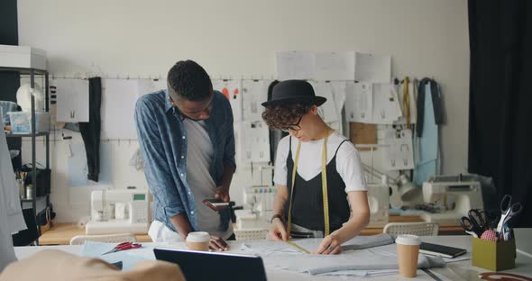 Female Dressmaker Measuring Fabric While African American Man Using Smartphone