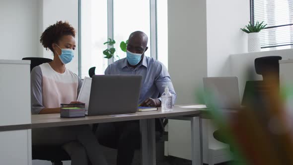 Diverse businessman and businesswoman in face masks discussing in office