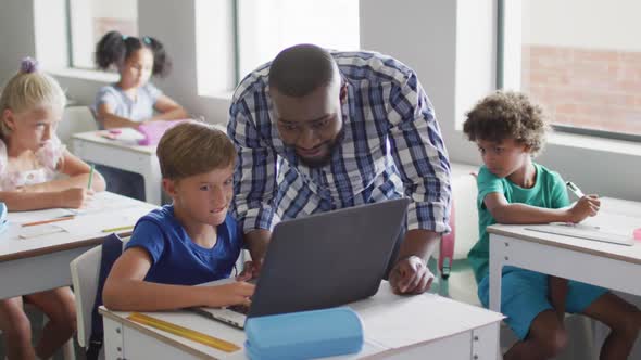 Video of happy african american male teacher helping caucasian boy with laptop