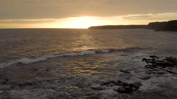 A low flying aerial shot along the ocean of Bass coast with the sunset on the horizon.