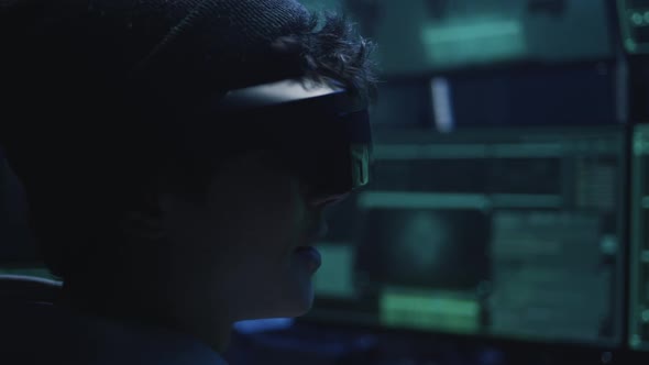 Young Hacker in VR Glasses Speaking in Dark Room