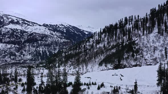 Aerial Fast Moving Shot of Huge Mountains Covered with Snow with Patches of Evergreen Tree in Solang