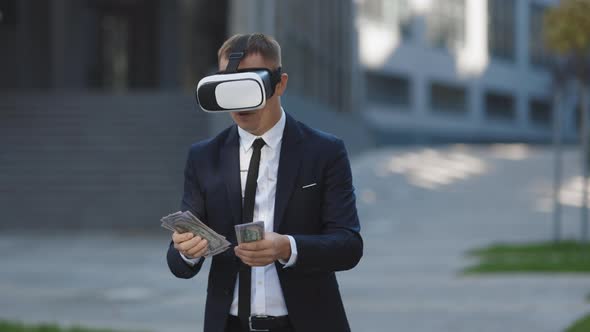 Rich Man Wearing Virtual Reality Headset Counting Money and Smiling Near Modern Office Building