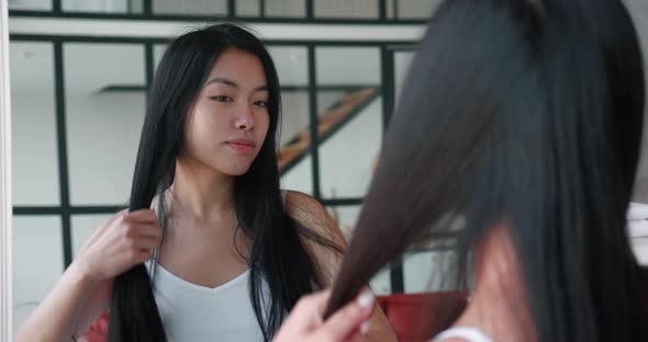 Beautiful Asian Woman Combing Her Long Hair with a Hair Brush Looking at Her Reflection in the