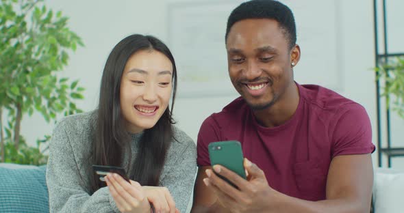 Attractive Young Mixed Ethnicity Couple with Smartphone and Credit Card Shopping on the Internet