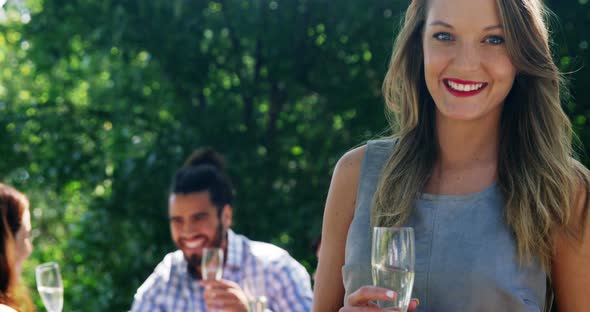 Portrait of woman standing with champagne glass while friends interacting in background