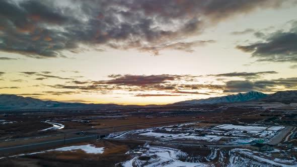 Aerial hyperlapse at sunset with clouds crossing the sky over the mountains and cars driving along t