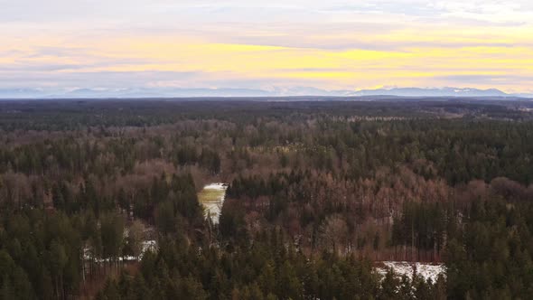 Idyllic house in the middle of a forest with the alp mountains in the background at sunset - zoomed