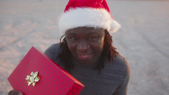 Happy Black Man with Santa Hat Holding Red Wrapped Christmas Gift