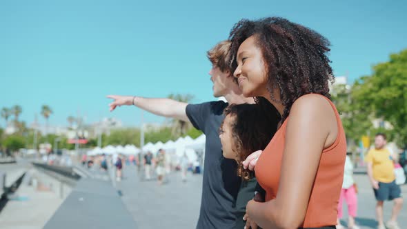 Cheerful multiethnic family talking and pointing on the embankment