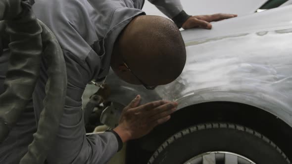 African American male car mechanic looking and rubbing the side of a car