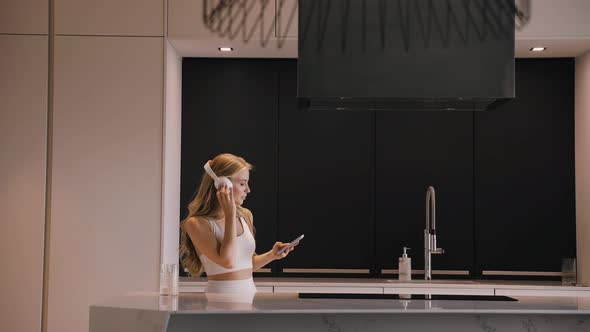 A Young Woman Dancing with a Phone in Her Hands and Headphones in the Kitchen