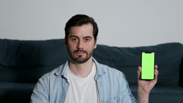 A young Man Looks at the Camera Shows a Smartphone with a Green Screen Integration