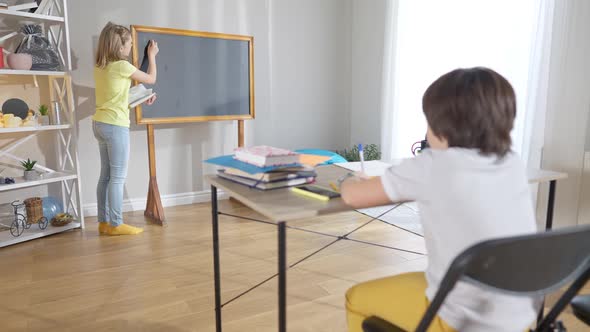 Wide Shot of Positive Confident Schoolgirl Writing on School Board As Blurred Schoolboy Sitting at