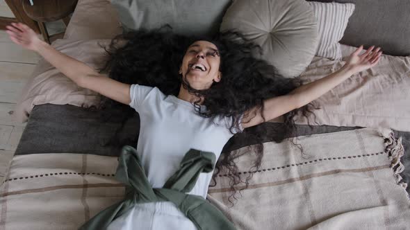 Top View Happy Young Funny Hispanic Woman Falls Down on Bed Lies in Cozy Bedroom Smiling Laughing