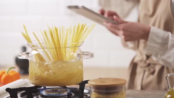 Hands Hold A Tablet In The Kitchen. Passionate About The Tablet While Cooking Spaghetti