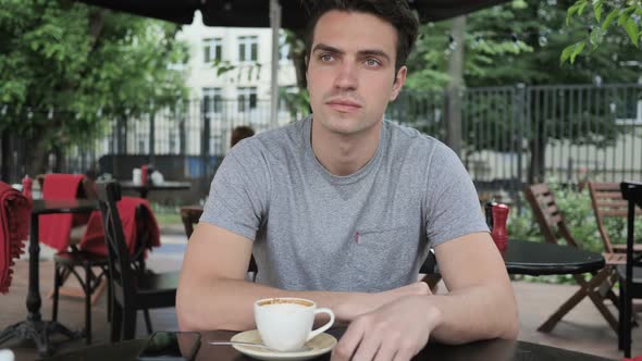 Young Man Sitting in Cafe Terrace and Looking Around