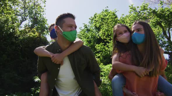 Caucasian couple wearing face mask carrying son and daughter on their back in the garden