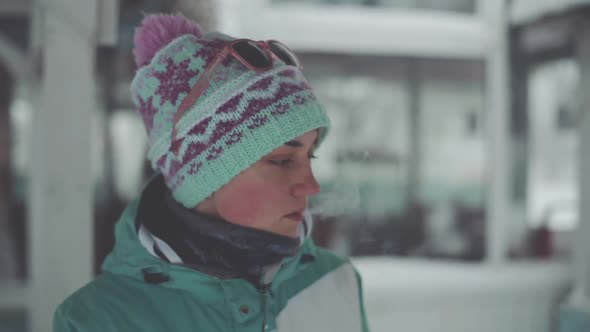 Young Attractive Woman Smokes a Cigarette in Winter in a Snow Park