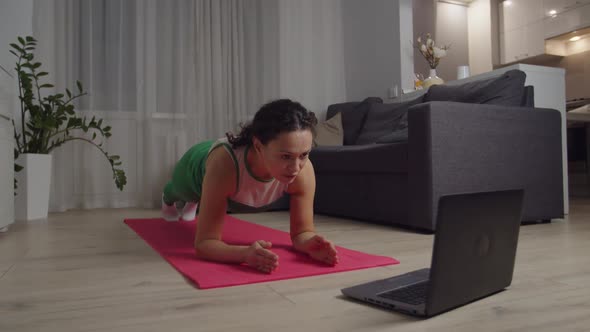 Woman Doing Plank Exercise Watching Video Tutorial on Laptop Indoors