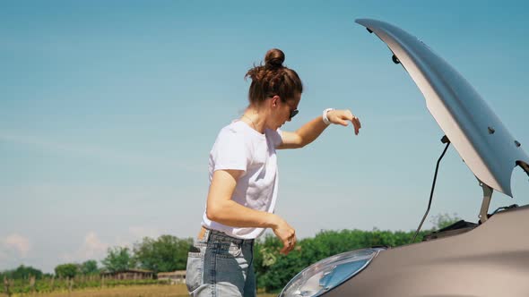 A Woman Opens the Hood of a Car and Looks at the Engine