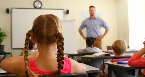 Multi-ethnic schoolkids raising hands while sitting at desk in a classroom at school 4k