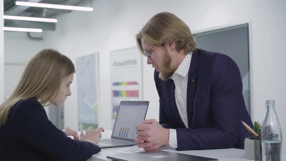 Young Bearded Man Trying To Cheer Up Female Colleague, Who Involved in Work on Netbook