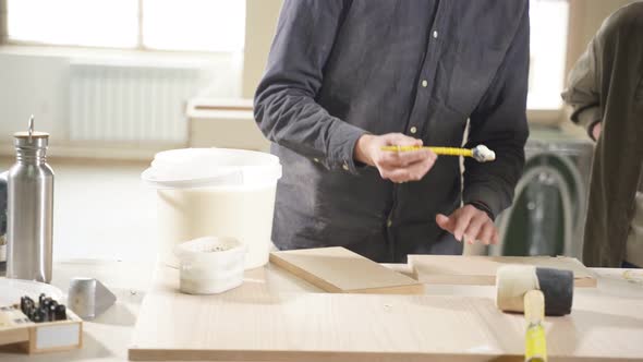 Carpenter Paints Wooden Slat for Production of Furniture on Table in Workshop