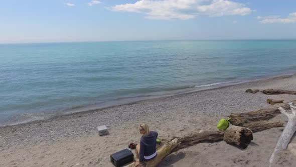 aerial pretty girl on a beach log rises quickly over water 4k