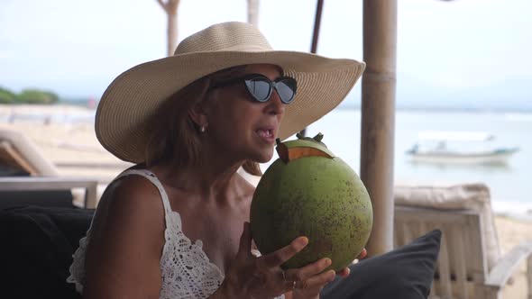 Caucasian Middleaged Woman Enjoying the Life By Drinking Coconut Milk From the Coconut on the Beach