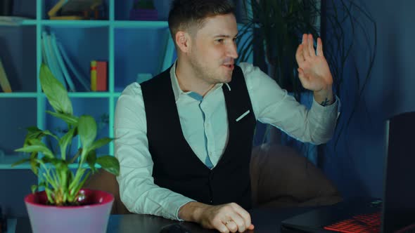 Young Man Conducts Live Broadcast on Computer Sitting in Armchair in Office