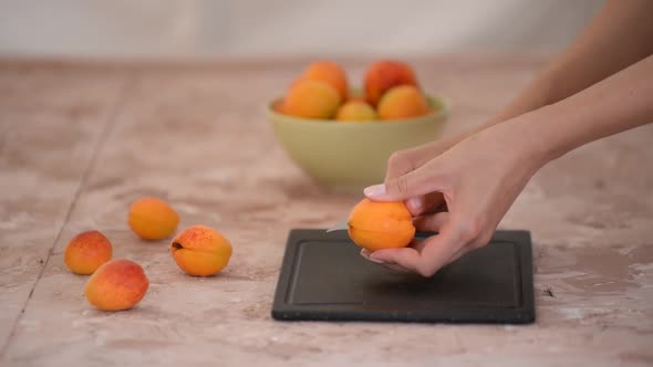 Female hands cutting fresh sweet apricot. Apricots slices on kitchen table.