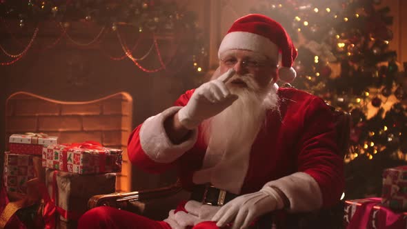 Kind Funny Santa Claus Is Sitting Alone at Room with Christmas Decorations at New Year Eve, Showing