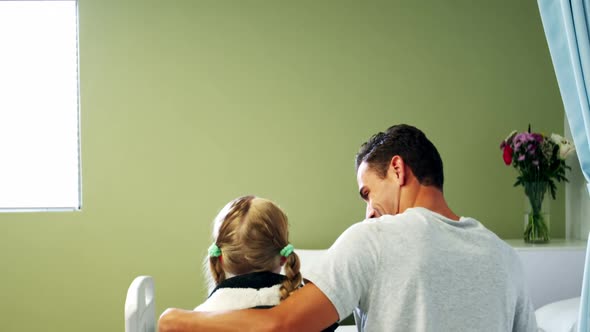 Father and daughter sitting on medical bed in hospital