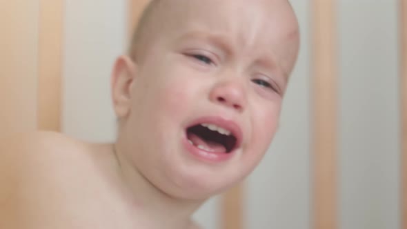 Portrait of Crying Screaming Naked Baby Infant Lying Sitting in Crib Cot Cradle