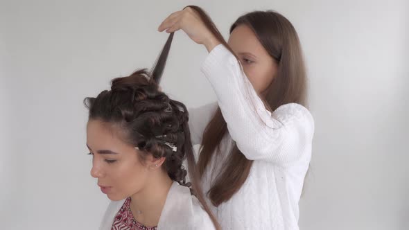 A hair stylist makes a hairstyle for a young beautiful girl with long dark hair